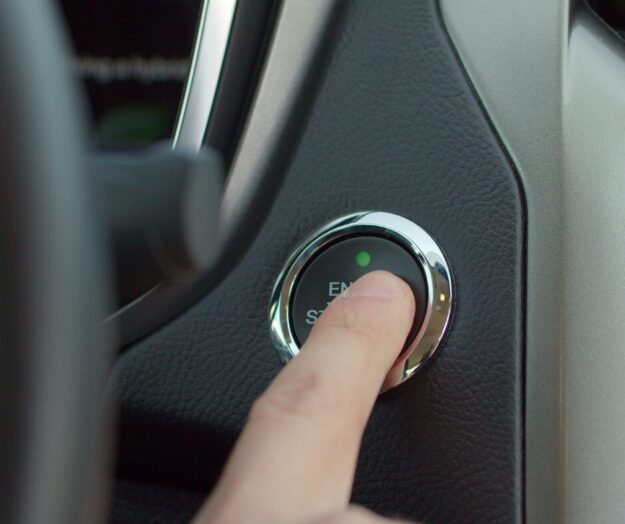Close-up of a person's hand holding a keyless entry fob with a car in the background.